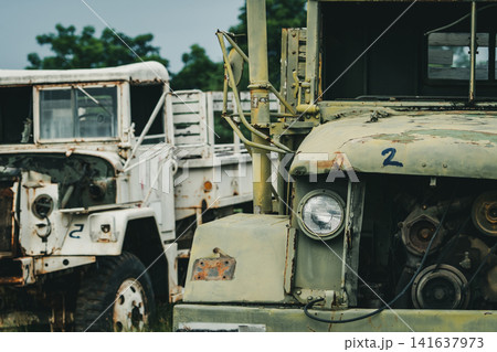 Abandoned rusty military trucks parked in storage yard with visible corrosion and aging equipment. Fleet depreciation, industrial maintenance, transportation logistics, recycling and economic decline. Abandoned rusty military trucks parked in storage yard with visible corrosion and aging equipment. Fleet depreciation, industrial maintenance, transportation logistics, recycling and economic decline. 141637973