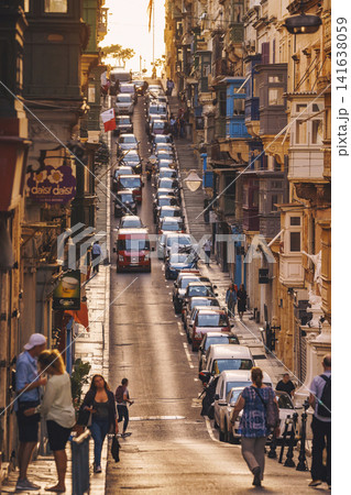 VALLETTA, MALTA - NOVEMBER 12, 2018 - Hilly ancient streets view with colourful balconies, people and cars in the medieval city VALLETTA, MALTA - NOVEMBER 12, 2018 - Hilly ancient streets view with colourful balconies, people and cars in the medieval city 141638059