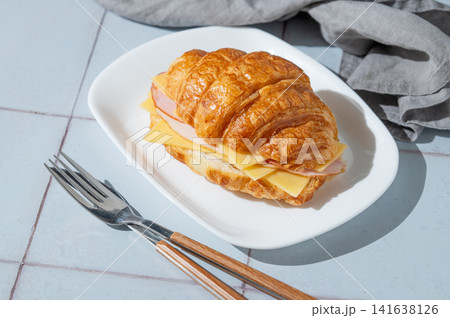 A golden croissant sandwich with ham and cheese on a white plate on a tile background 141638126