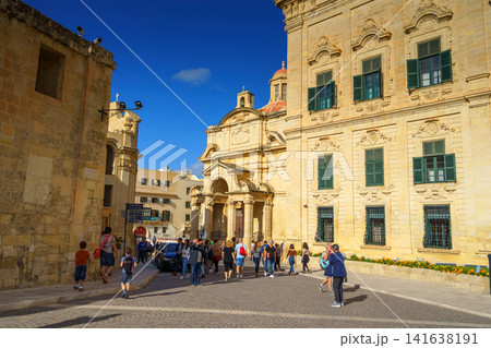 VALLETTA, MALTA - NOVEMBER 12, 2018 - Exterior view of the Auberge de Castille in Castille Square with people walking by VALLETTA, MALTA - NOVEMBER 12, 2018 - Exterior view of the Auberge de Castille in Castille Square with people walking by 141638191