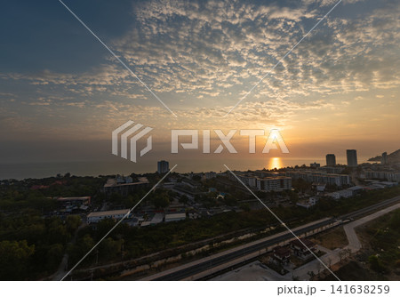 Golden sunrise over Hua Hin, Thailand, the sun reflecting across Gulf of Thailand. Condominiums and coastal buildings line shoreline beneath dramatic cloud filled morning sky. Golden sunrise over Hua Hin, Thailand, the sun reflecting across Gulf of Thailand. Condominiums and coastal buildings line shoreline beneath dramatic cloud filled morning sky. 141638259