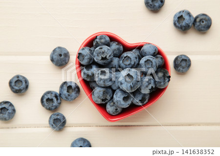 Blueberry in heart shaped bowl on light wooden background. Top view Blueberry in heart shaped bowl on light wooden background. Top view 141638352
