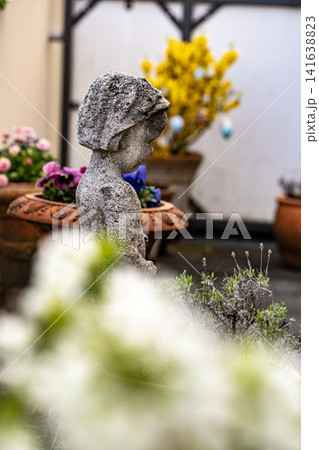 Stone Garden Statue Surrounded By Spring Flowers: Cozy Patio With Chrysanthemum And Geranium Plants Stone Garden Statue Surrounded By Spring Flowers: Cozy Patio With Chrysanthemum And Geranium Plants 141638823