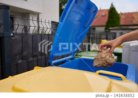 Woman placing paper packaging into blue recycling bin outside home 141638852