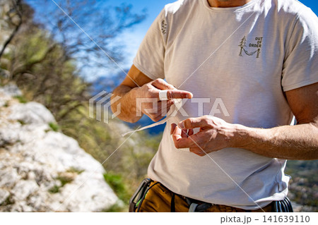 Male Climber Taping Fingers Before Route: Close Up Of Hands Preparing For Outdoor Rock Climbing Male Climber Taping Fingers Before Route: Close Up Of Hands Preparing For Outdoor Rock Climbing 141639110