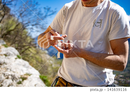 Male Climber Taping Fingers Before Route: Close Up Of Hands Preparing For Outdoor Rock Climbing 141639116