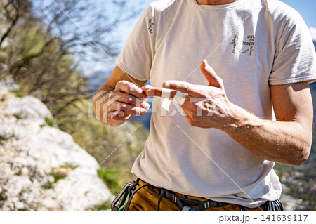 Male Climber Taping Fingers Before Route: Close Up Of Hands Preparing For Outdoor Rock Climbing Male Climber Taping Fingers Before Route: Close Up Of Hands Preparing For Outdoor Rock Climbing 141639117