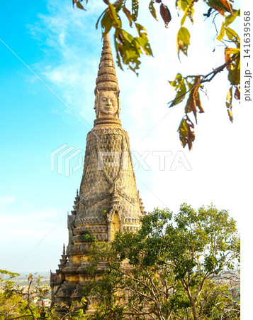 Ancient Stone Face Tower In Udong Cambodia: Historic Temple Monument Rising Above Lush Greenery At Golden Hour Ancient Stone Face Tower In Udong Cambodia: Historic Temple Monument Rising Above Lush Greenery At Golden Hour 141639568