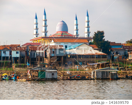 Riverside Mosque With Minarets On Mekong River In Cambodia: Islamic Architecture Reflected In Calm Water During Daytime Riverside Mosque With Minarets On Mekong River In Cambodia: Islamic Architecture Reflected In Calm Water During Daytime 141639570