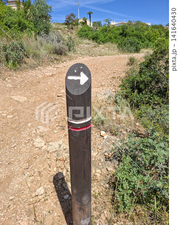 Trail marker post points the way on a sunny dirt path in a Mediterranean nature park 141640430