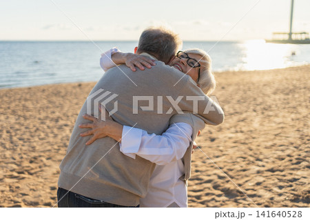 Senior mature couple hugging enjoying outdoor recreation walking on beach. Old husband wife embracing with tenderness love enjoying sweet bonding. Grandmother grandfather together. Family moment love Senior mature couple hugging enjoying outdoor recreation walking on beach. Old husband wife embracing with tenderness love enjoying sweet bonding. Grandmother grandfather together. Family moment love 141640528