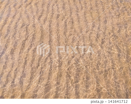 Crystal clear shallow ocean water flowing over golden ribbed sand, creating a serene, meditative ripple pattern. A calm nature scene, no people, capturing the peaceful essence of a summer beach. Crystal clear shallow ocean water flowing over golden ribbed sand, creating a serene, meditative ripple pattern. A calm nature scene, no people, capturing the peaceful essence of a summer beach. 141641712