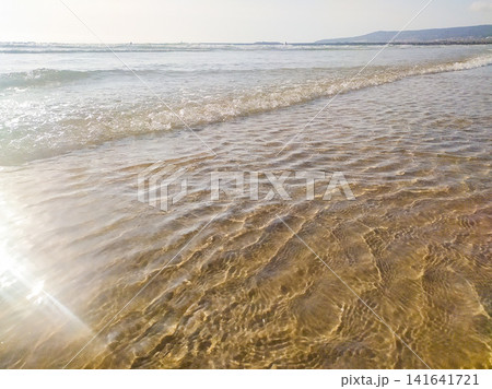 Gentle waves lap onto a pristine sandy shore at sunrise, evoking peace and serenity. This tranquil ocean landscape, with nobody present, offers a refreshing coastal escape for travel designs. 141641721