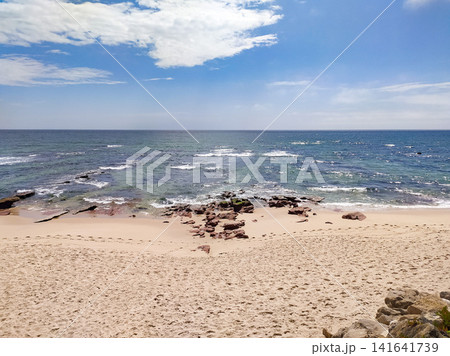 Serene beach landscape with rocky shore, footprints on sand, and vast blue ocean under a bright cloudy sky. Nobody. Evoking tranquility and peace, perfect for travel concepts. Serene beach landscape with rocky shore, footprints on sand, and vast blue ocean under a bright cloudy sky. Nobody. Evoking tranquility and peace, perfect for travel concepts. 141641739