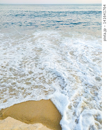 A tranquil view of white sea foam washing over golden sand under a calm blue ocean, evoking peace and deep relaxation. Perfect background for travel concepts. Nobody present. A tranquil view of white sea foam washing over golden sand under a calm blue ocean, evoking peace and deep relaxation. Perfect background for travel concepts. Nobody present. 141641764