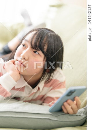 スマホを見る10代の女子中高生(リビング・うつ伏せ・笑顔・SNS・通信サービスイメージ) スマホを見る10代の女子中高生(リビング・うつ伏せ・笑顔・SNS・通信サービスイメージ) 141642127