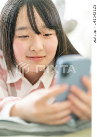 スマホを見る10代の女子中高生(リビング・うつ伏せ・笑顔・SNS・通信サービスイメージ) スマホを見る10代の女子中高生(リビング・うつ伏せ・笑顔・SNS・通信サービスイメージ) 141642128