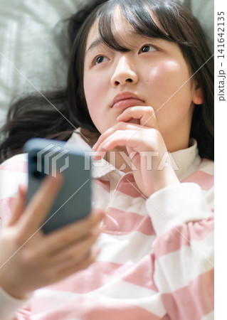 部屋でくつろぎスマートフォンをもつ中高生(Z世代・ライフスタイル・アプリ・広告素材) 部屋でくつろぎスマートフォンをもつ中高生(Z世代・ライフスタイル・アプリ・広告素材) 141642135