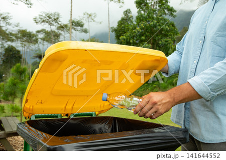 Person placing a plastic bottle into a yellow recycling bin 141644552