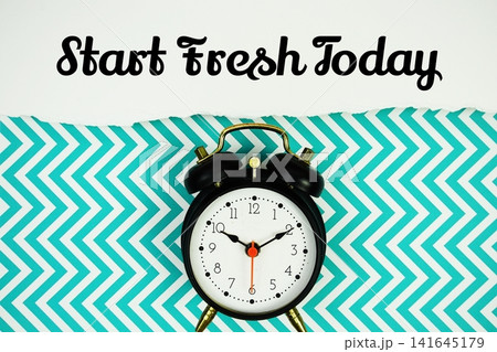 Start Fresh Today text written on paper with alarm clock on green chevron background Start Fresh Today text written on paper with alarm clock on green chevron background 141645179