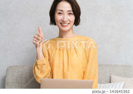 ソファーに座ってノートパソコンを使う女性 ライフスタイルイメージ ソファーに座ってノートパソコンを使う女性 ライフスタイルイメージ 141645362