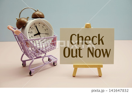 Check Out Now text with trolley shopping cart and alarm clock on pink background Check Out Now text with trolley shopping cart and alarm clock on pink background 141647832