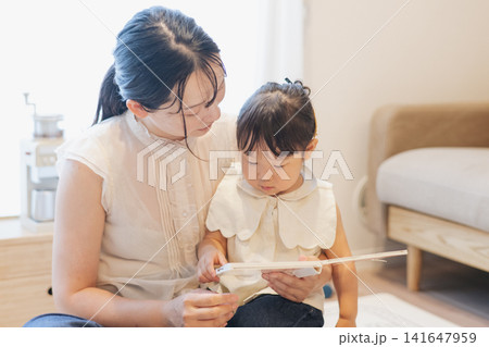 部屋の中で遊ぶ親子・読み聞かせ・子育てイメージ・絵本を読む女の子と母親 部屋の中で遊ぶ親子・読み聞かせ・子育てイメージ・絵本を読む女の子と母親 141647959