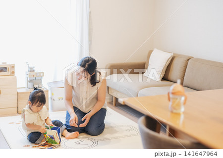 部屋の中で遊ぶ親子・読み聞かせ・子育てイメージ・絵本を読む女の子と母親 141647964