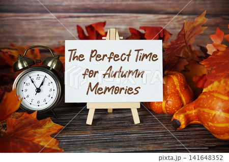 The Perfect Time for Autumn Memories text with alarm clock, maple leaf and pumpkins decoration on wooden background The Perfect Time for Autumn Memories text with alarm clock, maple leaf and pumpkins decoration on wooden background 141648352