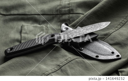 A tactical black knife with textured micarta handle and sheath rests on olive green fabric 141649232