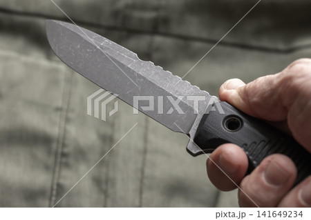 Close-up of a hand gripping a tactical fixed-blade knife, showing textured handle Close-up of a hand gripping a tactical fixed-blade knife, showing textured handle 141649234