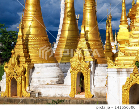 Golden Buddhist pagodas at Inle Lake, Myanmar, symbol of spiritual travel and cultural immersion, ancient stupas glowing in afternoon light under dramatic sky in Shan State 141650300