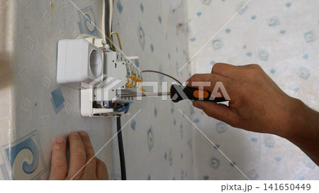 A man's hands using a screwdriver to install a modular circuit breaker into an electrical panel. The technician carefully tightens the terminal, connecting the copper wire to ensure safe operation A man's hands using a screwdriver to install a modular circuit breaker into an electrical panel. The technician carefully tightens the terminal, connecting the copper wire to ensure safe operation 141650449