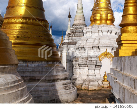 Golden Buddhist pagodas at Inle Lake, Myanmar, symbol of spiritual travel and cultural immersion, ancient stupas glowing in afternoon light under dramatic sky in Shan State 141650506