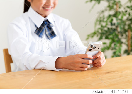 リビングのテーブルでスマホを見る制服姿の中学生 リビングのテーブルでスマホを見る制服姿の中学生 141651771