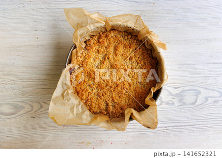 Overhead view of a whole homemade cherry crumb cake with golden streusel topping in a parchment lined metal springform pan on a wooden table Overhead view of a whole homemade cherry crumb cake with golden streusel topping in a parchment lined metal springform pan on a wooden table 141652321
