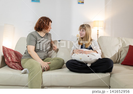 Mother and daughter talking on sofa at home Mother and daughter talking on sofa at home 141652956