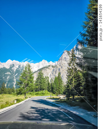 Stunning view on the Vrsic Pass in Triglav National Park, Slovenia, looking towards the rocky Julian Alps mountains with winding alpine road, green slopes and dramatic sky 141654199
