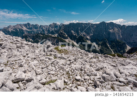 View from the middle Ponza mountain in Triglav National Park, Slovenia, looking over white rocky alpine valley routes and steep Julian Alps peaks with narrow hiking trails and dramatic mountain landsc 141654213