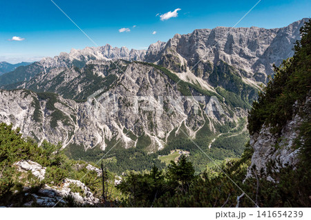 Mountain views with nature on the hike to the Ponza mountains in Triglav National Park, Slovenia, with rocky Julian Alps peaks, green alpine meadows and forested slopes under dramatic sky 141654239