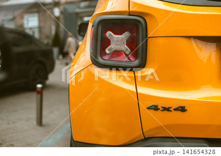 Close up detail of bright yellow compact SUV with 4x4 badge parked on urban street. Modern automotive design, contemporary city mobility and stylish crossover vehicle concept. Car trip. Urban scene. 141654328