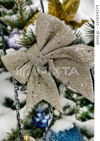 A decorated Christmas tree stands in a winter setting with snow around. Colorful ornaments hang from branches. A large bow is placed on the tree A decorated Christmas tree stands in a winter setting with snow around. Colorful ornaments hang from branches. A large bow is placed on the tree 141654374