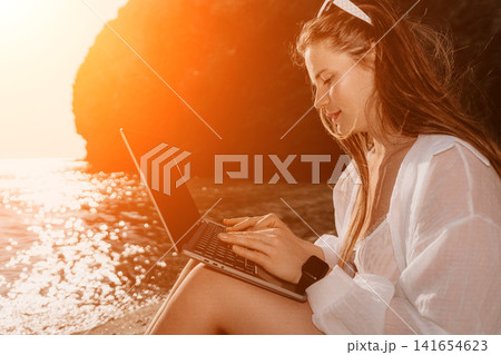 Laptop freelancer beach young woman working remotely on her computer outdoors at sunset during vacation for digital nomad lifestyle 141654623