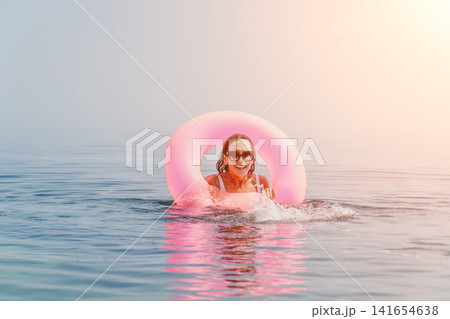 Woman swimming inflatable joyful adult female wearing sunglasses floating with pink inner tube in calm blue sea water during sunny summer vacation Woman swimming inflatable joyful adult female wearing sunglasses floating with pink inner tube in calm blue sea water during sunny summer vacation 141654638