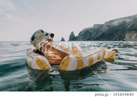 Woman Inflatable Float Sea Relaxing on a Striped Inflatable Float in the Ocean Woman Inflatable Float Sea Relaxing on a Striped Inflatable Float in the Ocean 141654640