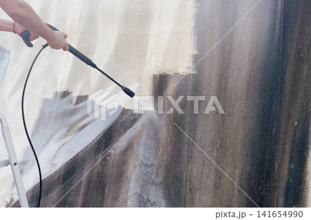 Side view of worker hand holding high pressure washer lance to clean dirty white tarp canvas fabric for industrial professional wash stock photo background Side view of worker hand holding high pressure washer lance to clean dirty white tarp canvas fabric for industrial professional wash stock photo background 141654990
