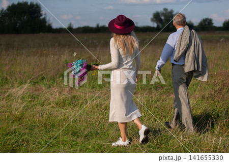 Couple enjoys a peaceful walk in a field during a sunny afternoon, celebrating nature and togetherness Couple enjoys a peaceful walk in a field during a sunny afternoon, celebrating nature and togetherness 141655330