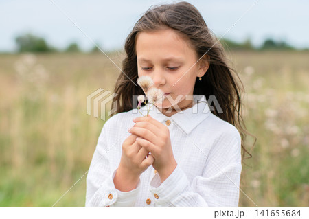 Young girl enjoying a moment in nature while holding a delicate flower in a serene field on a cloudy day Young girl enjoying a moment in nature while holding a delicate flower in a serene field on a cloudy day 141655684