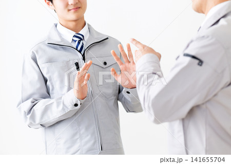 怒られるのを嫌がる作業着を着た若い男性と部下を注意をするミドル男性 怒られるのを嫌がる作業着を着た若い男性と部下を注意をするミドル男性 141655704