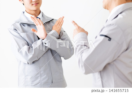 怒られるのを嫌がる作業着を着た若い男性と部下を注意をするミドル男性 141655715